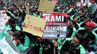 Driver GrabBike membentangkan poster bertuliskan Naikkan Argo 2.500/km, Tolak Penerimaan Baru!!!, dan Kami Rakyat Indonesia Bukan Rakyat GrabBike.