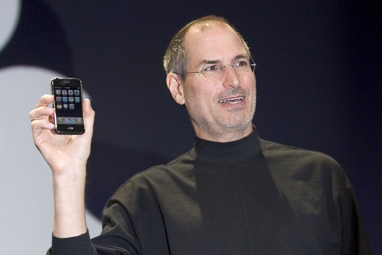 Peluncuran iPhone pertama SAN FRANCISCO, CA - JANUARY 9: Apple CEO Steve Jobs holds up the new iPhone that was introduced at Macworld on January 9, 2007 in San Francisco, California. During the keynote Jobs introduced the new iPhone which will combine a mobile phone, a widescreen iPod with touch controls and a internet communications device with the ability to use email, web browsing, maps and searching. The iPhone will start shipping in the US in June 2007. (Photo by David Paul Morris/Getty Images)