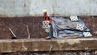 Seorang pekerja memasang konblok di dinding sungai Ciliwung.