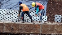 Dua orang pekerja memasang konblok di dinding sungai Ciliwung.