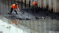 Pasukan oranye mengeruk lumpur menggunakan cangkul.