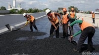 Pekerja menghamparkan material aspal.