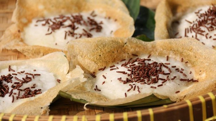 Serabi Solo, pancakes using coconut milk, a popular snack and breakfast item from city of Solo in Central Java region. These are the variant that add some chocolate sprinkles for some chocolatey flavor. These pancakes have thin, wide other rim as they are cooked in woks; which also caused the center part being the thickest and meatiest part. The pancakes are underlined with cut pieces of banana leaves to prevent them from sticking to the tray. A traditional woven bamboo tray is used as the base. This image was taken outdoor and used sunlight as its natural lighting source.