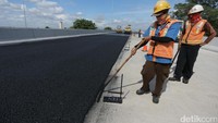 Pekerja meratakan lapisan aspal.