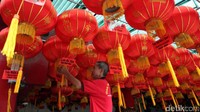 Seorang pekerja sedang memasang lampion di depan klenteng.