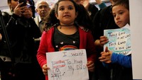 Bocah perempuan berusia tujuh tahun bernama Teija, terlihat memamerkan poster bahwa ia ingin memeluk sang ayah yang terjebak di Iran karena larangan perjalanan. REUTERS/Ted Soqui.