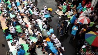 Massa pro Habib Rizieq Syihab menggunakan jas hujan sebagai alas salat, tampak pula peserta yang menggunakan kardus.