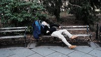 Seorang pria tengah bersandar bangku taman Manhattan dengan cuaca hangat pada Rabu (8/2). Tetapi keesokan harinya salju mulai menutupi lokasi. Spencer Platt/Getty Images.