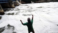 Warga melemparkan jala ke Banjir Kanal Timur, Marunda yang penuh busa akibat limbah.