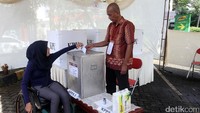 Seorang disabilitas memasukan kertas suaranya setelah melakukan pencoblosan.