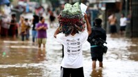 Warga melintas di jalanan yang terendam banjir. Berdasarkan data sementara yang dihimpun Pusdalops BPBD DKI Jakarta tercatat banjir merendam permukiman di bantaran Sungai Cilwung dan sebagian Kali Cipinang.