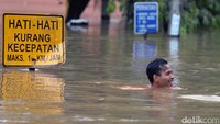 Seorang warga berjalan di genangan air yang mencapai lehernya.