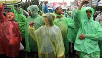 Mereka menggelar aksi dengan memakai jas hujan.