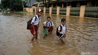 Beberapa pelajar SD terlihat melintasi banjir dengan mengangkat sepatu dan menggulung celana.