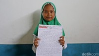 Seorang anak memperlihatkan surat yang ditulisnya untuk presiden di depan kamera.