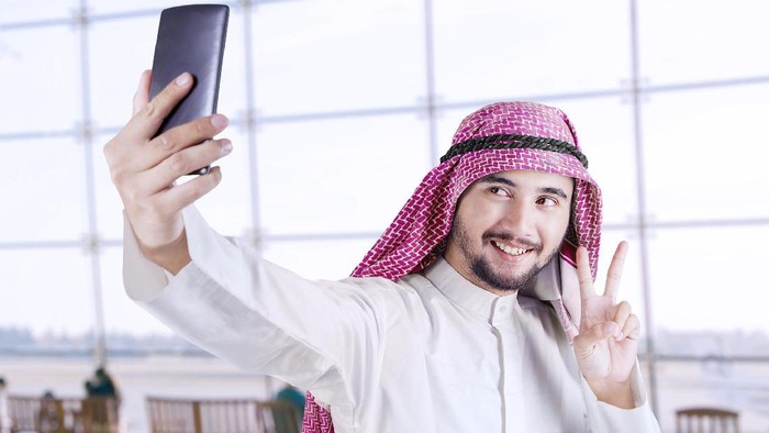 Portrait of Arabian tourist using a smartphone to take selfie picture in the airport