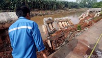 Seorang warga melintas di samping dinding sungai yang ambrol.