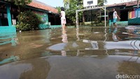 Dua orang anak bermain di halaman sekolah yang terendam banjir.