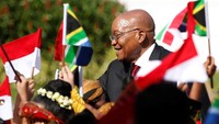 Puluhan anak sekolah dasar yang mengenakan pakaian adat mengibarkan bendera Indonesia dan Afrika Selatan untuk menyambut kedatangan Jacob Zuma. Pool/Darren Whiteside/Reuters/detikFoto.