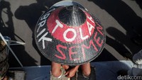 Sambil duduk di kursi besi di depan pintu Monas yang berhadapan dengan Istana Merdeka, mereka menggelar aksi protes dalam diam. Hanya topi caping bertulisan Tolak Pabrik Semen yang menjadi suara penolakan mereka.
