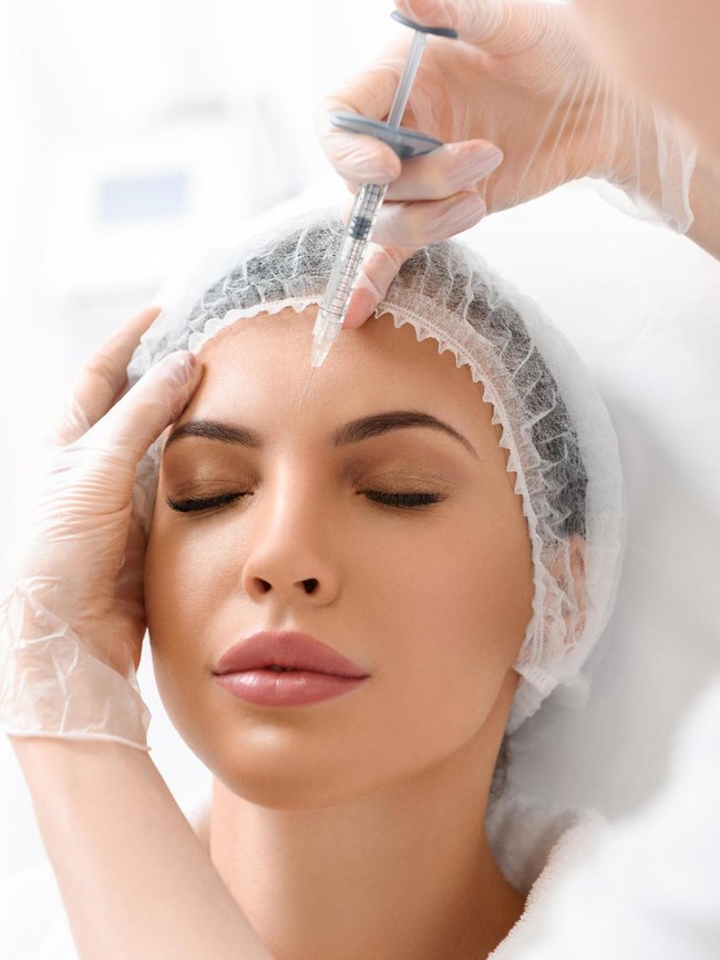 Beautiful young woman gets beauty injection in forehead from sergeant. Isolated over white background.