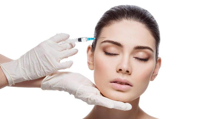 Beautiful young woman gets beauty injection in forehead from sergeant. Isolated over white background.