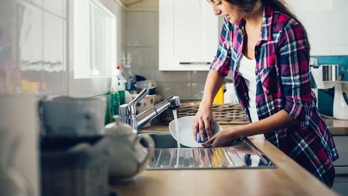 Young couple cleaning kitchen together. Focus is on smiling woman.