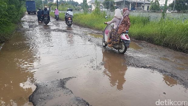 Warga melintas di jalan yang rusak