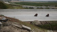 Tampak anak-anak dengan sepeda motor melintas di jalan tol yang tengah dikerjakan.