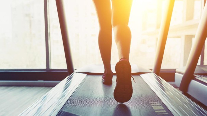 Fitness girl running on treadmill. Woman with muscular legs in gym