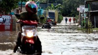 Pengendara mendorong motornya yang mogok akibat menerobos banjir di kawasan tersebut.