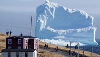 Gunung es yang tampak begitu besar di permukaan laut belakang rumah penduduk. Traveler pun banyak yang penasaran untuk melihatnya langsung (Jody Martin/Reuters)