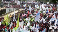 Massa aksi dari berbagai organisasi buruh mengibarkan bendera dan membentangkan spanduk tuntutan.