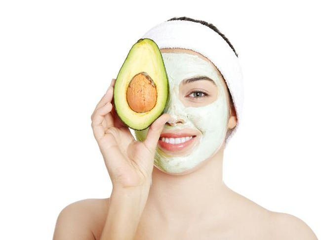Beautiful woman with clay facial mask and avocado. isolated on white