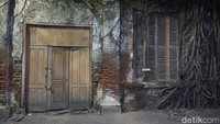 Traveler akan menemukan sebuah rumah tua yang panjang, kusam dan terlihat tak lengkap karena sudah tak ada atapnya. Di tengah rumah akan ada sebuah pohon besar yang akarnya menempel ke dinding (Bonauli/detikTravel)