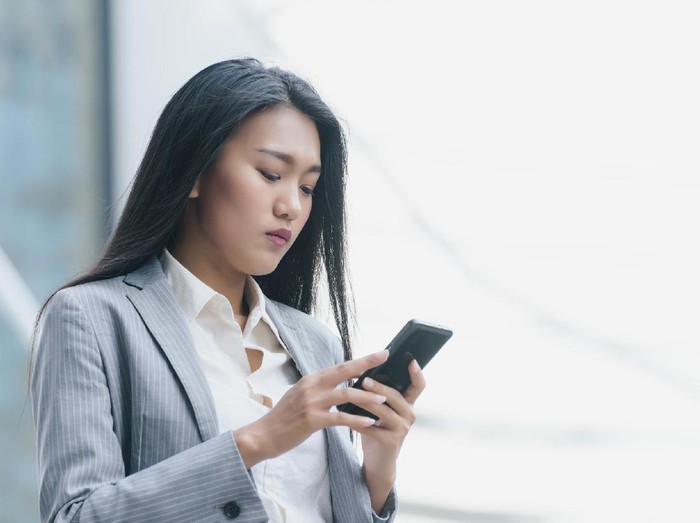 671064686 Beautiful young business woman browsing wireless on cell telephone during work break,female financier chatting on her mobile phone while standing in the city