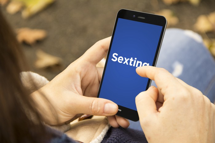 closeup of a young caucasian woman face down in bed using a smartphone