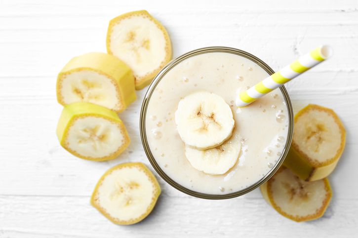 Glass of banana smoothie on white wooden background from top view
