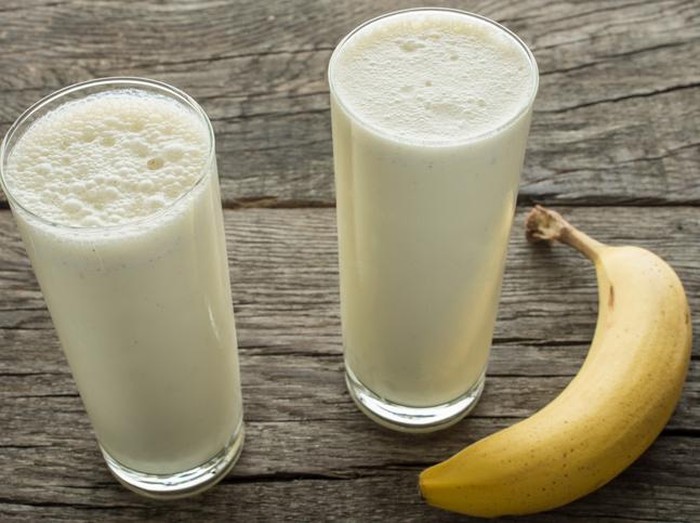 Glass of banana smoothie on white wooden background from top view