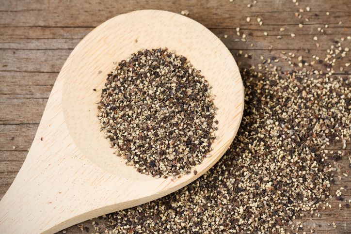 Coarse ground black pepper on a wooden spoon and spilled on an old, weathered wood surface.