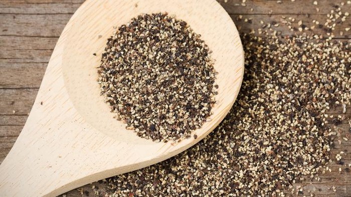 Coarse ground black pepper on a wooden spoon and spilled on an old, weathered wood surface.