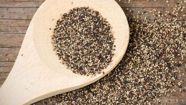 Coarse ground black pepper on a wooden spoon and spilled on an old, weathered wood surface.