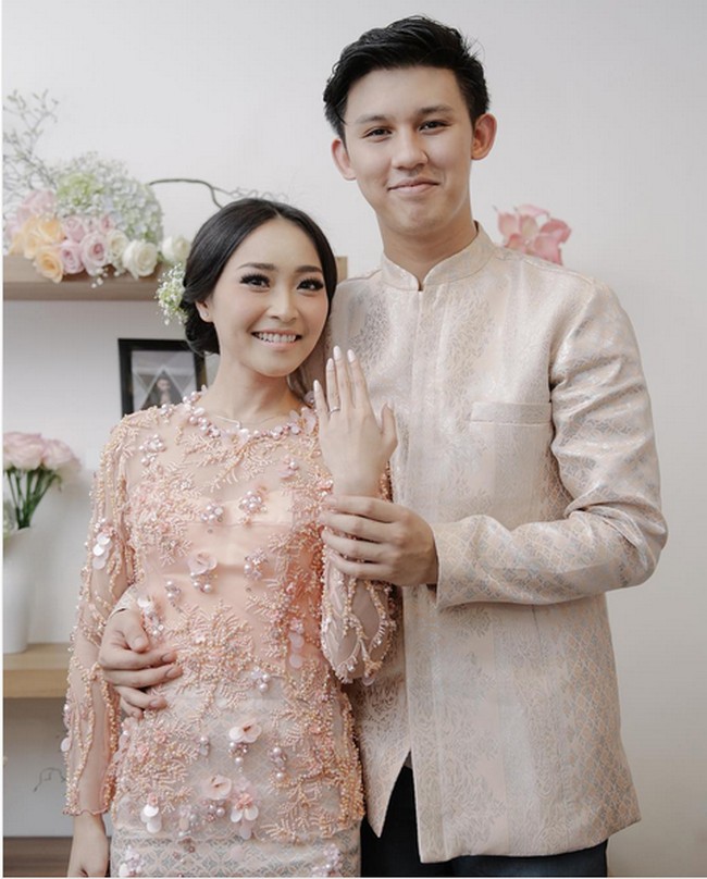 Rinni Wulandari tampil lebih kasual di hari pertunangannya. Nuansa kebaya peach dipercantik detail bordir, dan payet 3D membuat tampilan kebaya terasa modern. Rinni hari itu memadukan model kebaya rancangan Titis Sapoetra Bridal bersama songket metalik yang dijadikan rok pendek sehingga suasana lamaran terasa playful. Foto: Instagram/Rinni Wulandari