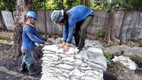 Lumpur dikeruk dan dimasukkan ke karung.