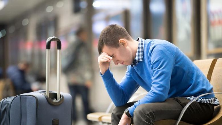 jet lag Portrait of young handsome guy wearing casual style clothes waiting for transport. Tired traveler man travelling with suitcase sitting with frustrated facial expression on a chair in modern station