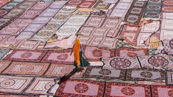 Seorang wanita ala Rajasthani yang sedang berjalan melintasi lautan tekstil yang ditata kering di India Utara. Karya fotografer Callie Chee. (Foto: National Geographic/Callie Chee)