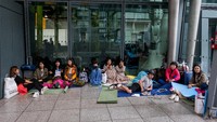 Dari live report BBC terlihat gambar yang menunjukkan tas-tas, koper, barang bawaan para penumpang memenuhi lantai bandara. Para penumpang pun juga terlihat antre di depan meja informasi untuk mencari tahu penyebab pembatalan penerbangan. Jack Taylor/Getty Images.