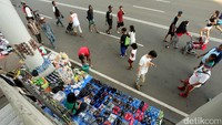 Penjual sandal, minuman dan mainan menggelar lapak di antara pilar halte busway. 
