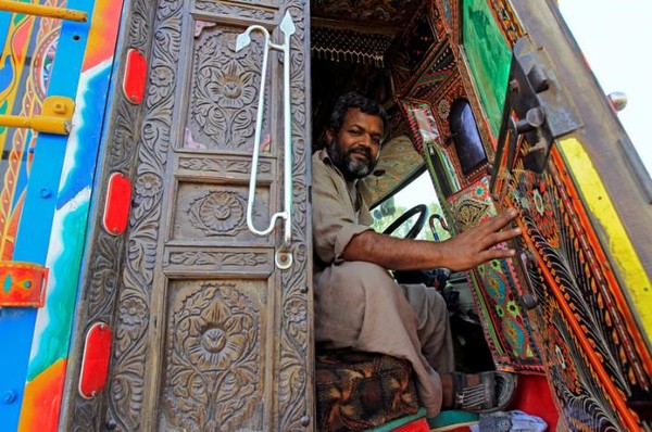 Pengemudi truk berpose sembari memegang pintu kayu truk yang berukir. Cantik ya truknya! (Caren Firouz/REUTERS) Pengemudi truk berpose sembari memegang pintu kayu truk yang berukir. Cantik ya truknya! (Caren Firouz/REUTERS)