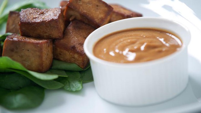tahu bacem Indonesian marinaded tofu with peanut satay sauce on a small bed of spinach.
